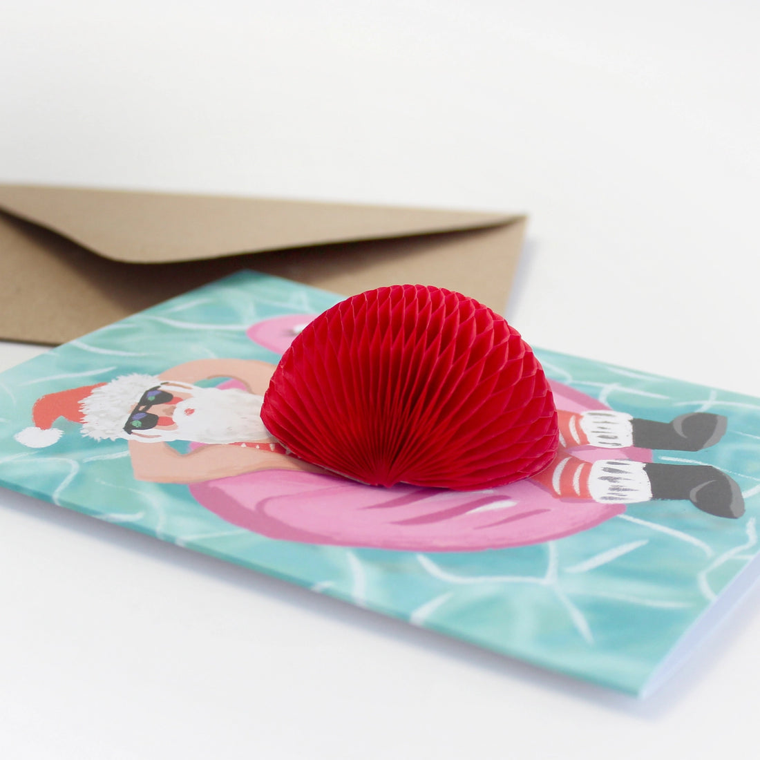 Christmas greeting card featuring Santa relaxing on a pink flamingo float with a 3D red honeycomb belly – Funky Confetti