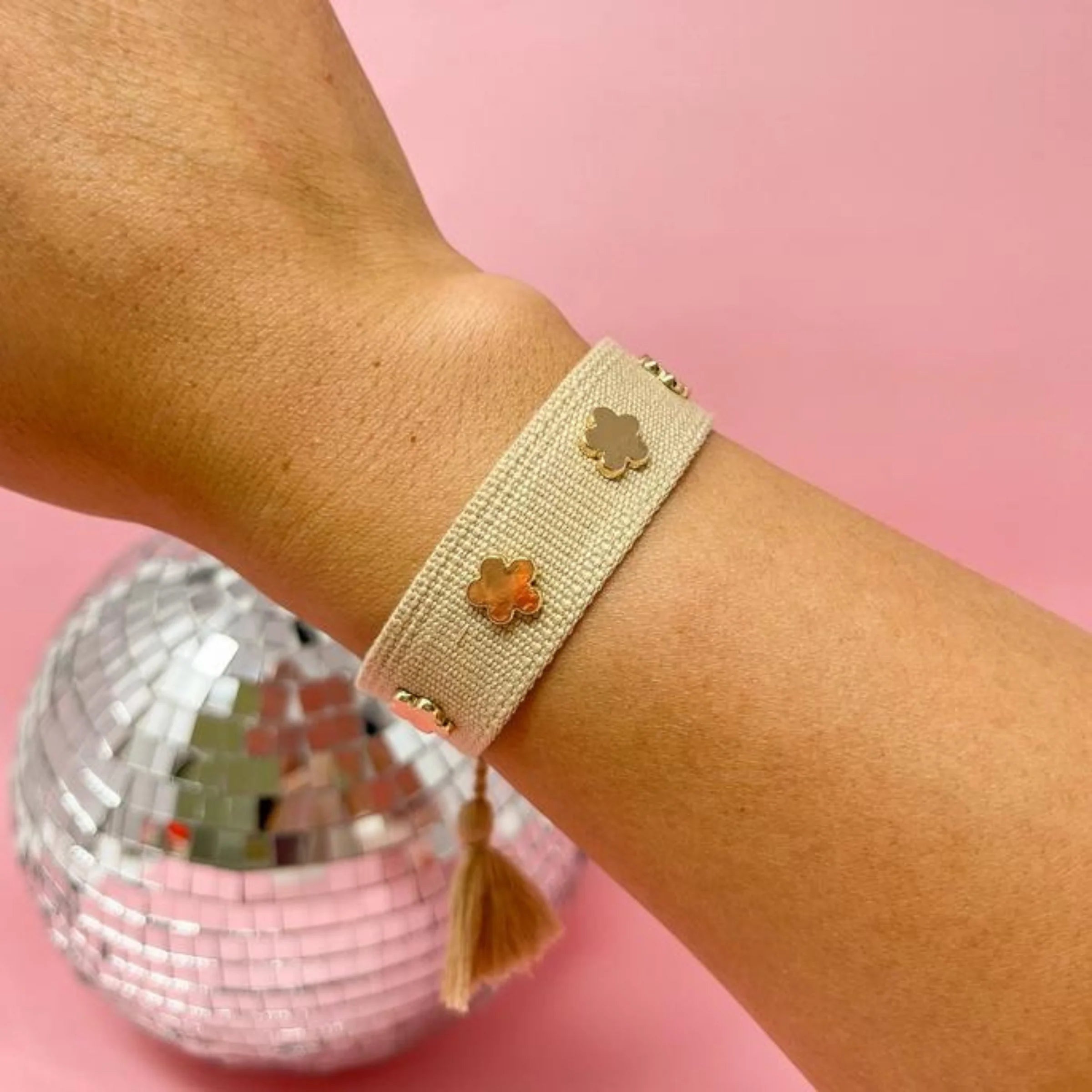 Tan adjustable woven bracelet with gold flower charms and tassel ends