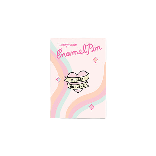 Heart-shaped “Regret Nothing” enamel pin on backing card with pastel rainbow design.